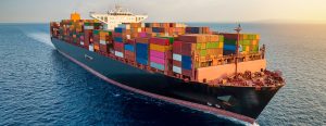 Aerial view of a full container load cargo ship traveling over open ocean during sunset time